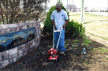 Man operating tiller preparing garden bed for flowers